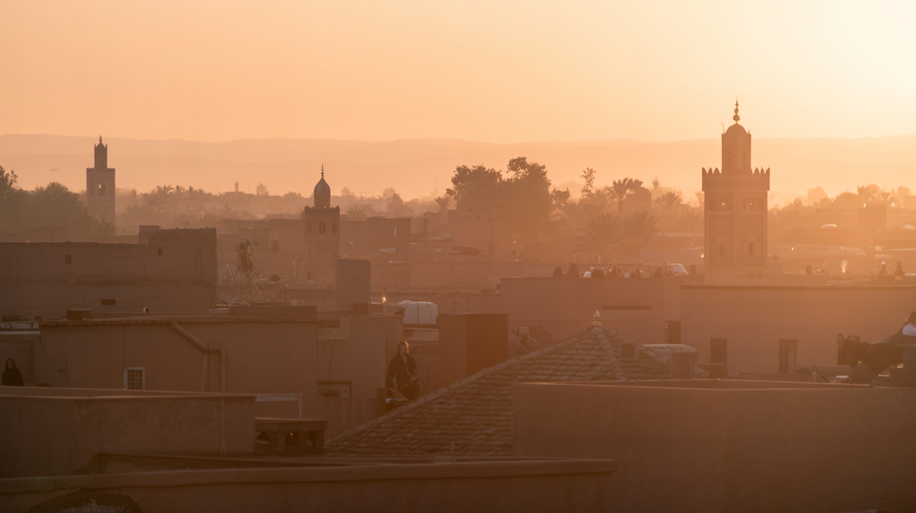 Marrakech medina rooftops at first light, silhouettes of minarets against warm golden sky